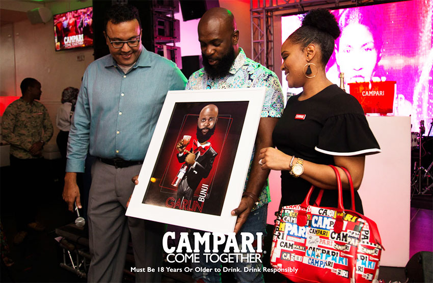 Image of Campari Caribbean’s Regional Commercial Director Michelle Brown (right) presenting Bunji Garlin with his animated Campari Red Image.