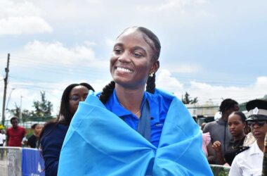 Julien Alfred draped in a Saint Lucia Flag beams at the crowd at the Hewanorra International Airport enroute to Castries