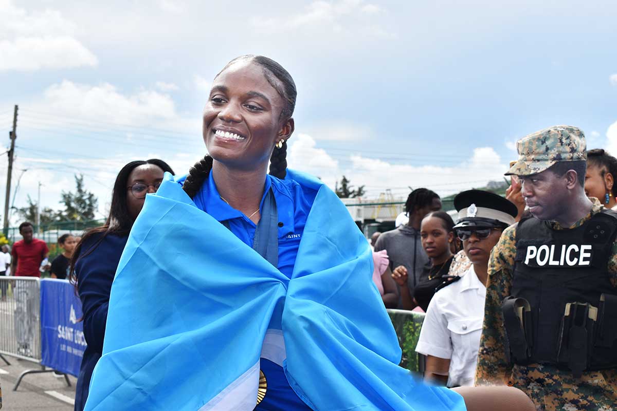 Julien Alfred draped in a Saint Lucia Flag beams at the crowd at the Hewanorra International Airport enroute to Castries